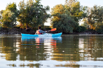 Fototapeta premium Woman kayaking on blue kayak in summer Danube river near trees