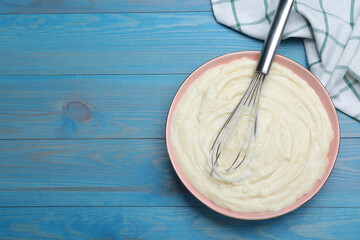 Pastry cream with balloon whisk on light blue wooden table, flat lay. Space for text