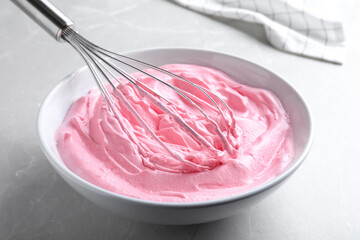 Whipping pink cream with balloon whisk on light grey table, closeup