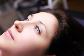 a model girl with blue eyes is lying on a permanent makeup procedure her eyebrows are being prepared for powder spraying - obrazy, fototapety, plakaty