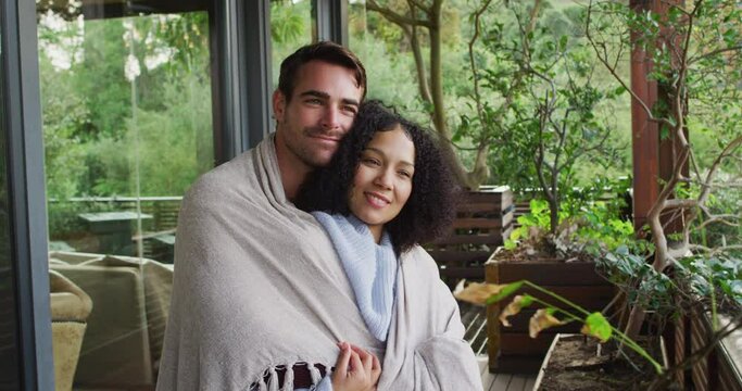Smiling mixed race couple wrapped in sheets embracing each other in the balcony at vacation home
