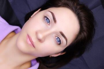 a model girl with blue eyes lies on a cosmetology couch with her eyebrows tattooed - obrazy, fototapety, plakaty
