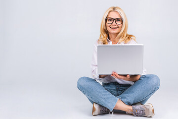 Naklejka premium Business concept. Portrait of happy senior aged woman in casual sitting on floor in lotus position and holding laptop isolated on white background. Copy space for text.