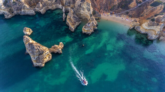 Camilo Beach in Lagos, Algarve - Portugal. Portuguese southern golden coast cliffs. Tourists on the beach. Sunny day aerial view.