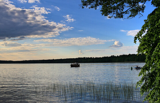 Motorboat running on the lake. In the background a dark forest. Blue sky with white clouds. The reeds are reflected in the water. Necko Lake in Augustow. A warm summer afternoon 