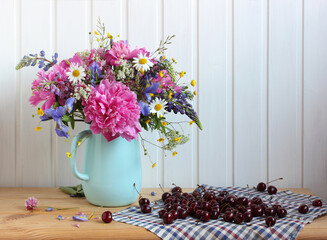 flowers and herbs in a jug and cherries on the table.