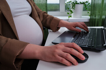 Hands of a pregnant woman typing text on a computer keyboard