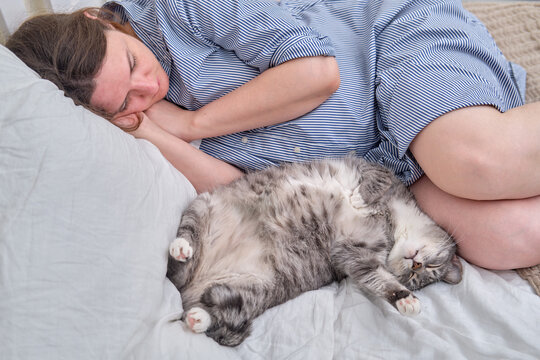 A pregnant woman and a gray cat sleep on a bed during the day - Powered by Adobe