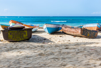 Dramatic image of old wooden weathered fishing boats on the Caribbean coast with turquoise blue water and white sandy beach.