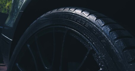 Close up of washing wheel tyre with spraying soapy water in car wash. Exterior car detailing concept