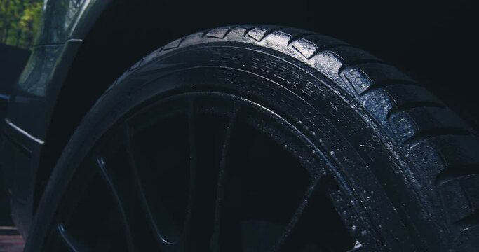 Close up of washing wheel tyre with spraying soapy water in car wash. Exterior car detailing concept