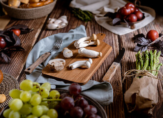 Dark photography of mushrooms, asparagus, bread, garlic and plums on a table of old wood. Vegetables recipe of for autumn or winter. Moody picture of seasonal cultivated fungus on a wooden table.
