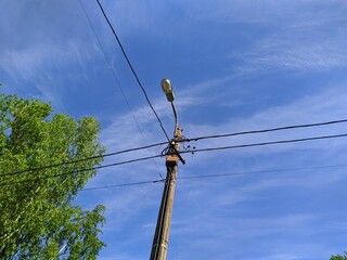electric pole with wires against the blue sky and green trees