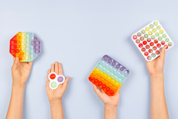 Many hands holding colorful pop it fidget toys on blue background. Push pop-it fidgeting game helps relieve stress, anxiety, autism, provide sensory and tactile experience for children