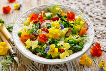 Vegan vegetable salad with edible pansy flowers in a white ceramic bowl fokus on the flower inside, close up view. Healthy eating concept
