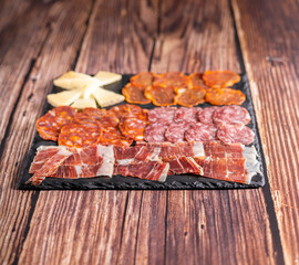 Food photography of chorizo, salami, ham, cheese and other appetizers on a dark board. Typical spanish tapas meal on a wooden table.