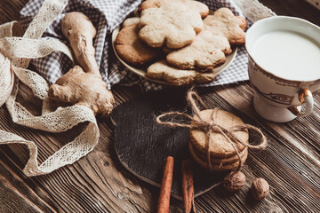 Close up of homemade ginger cookies, cinnamon, ginger with cup of milk on a towel wooden table. Copy space. Retro toned image, flat lay