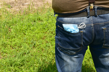 Man keeps a protective medical mask against coronavirus infection (COVID-19) in the back pocket of his jeans