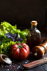 Healthy salad ingredients - fresh organic lettuce and tomatoes, a bottle with vegetable oil and spices on an old wooden table, low key photo