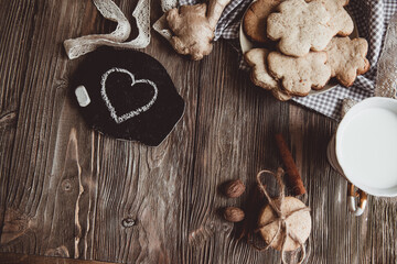 Close up of homemade ginger cookies, cinnamon, ginger with cup of milk on a towel wooden table. Copy space. Retro toned image, flat lay