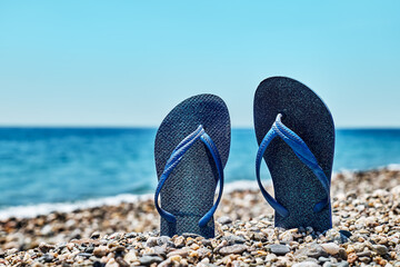Blue flip-flops on the pebble beach with turquoise sea and blue sky in background. Summertime....