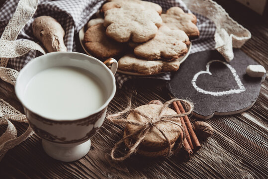 Close up of homemade ginger cookies, cinnamon, ginger with cup of milk on a towel wooden table. Copy space. Retro toned image, flat lay