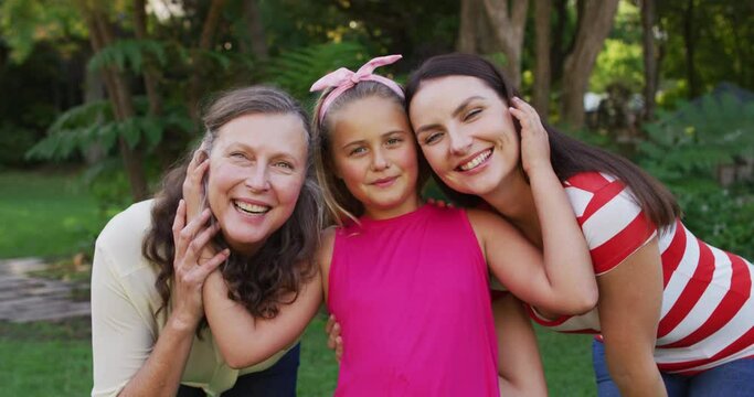 Portrait of happy caucasian grandmother, granddaughter and mother embracing in garden and smiling