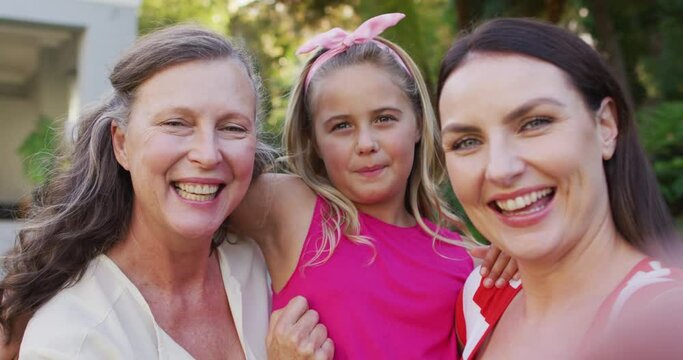 Portrait of happy caucasian grandmother, granddaughter and mother embracing in garden and smiling