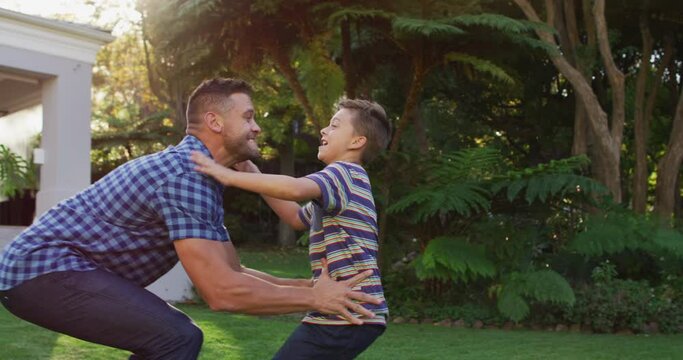 Happy caucasian son running and jumping into the arms of father in garden