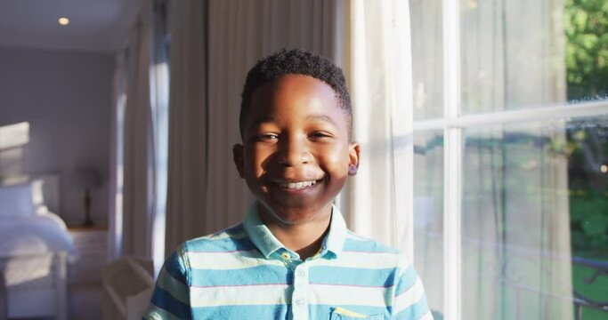 Portrait of happy african american boy looking out of sunny window, turning to camera and smiling