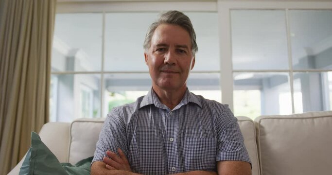 Smiling senior caucasian man sitting in living room, listening during a video call