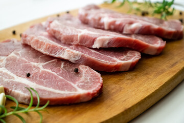 Sliced raw pork meat with fresh rosemary and pepper on cutting board