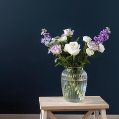 Bouquet of hackelia velutina, purple and white roses, small tea roses, matthiola incana and blue iris in glass vase opposite on black background