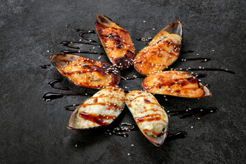 Shellfish mussels Baked with cheese in a shell on a black stone. Grilled mussels with teriyaki sauce and sesame seeds.