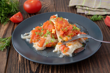 Fish stew with tomatoes and dill on the plate on wooden table. Plaice fillet and cooked vegetables for healthy dinner.