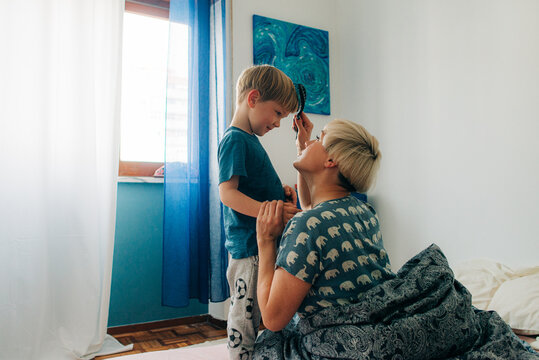 Mother brushing her son while sitting in bed