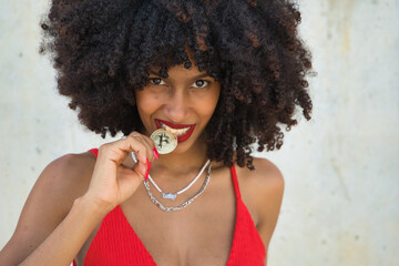 Young, beautiful African-American woman biting a cryptocurrency on a gray cement background.