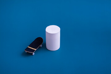 Finger skateboard on a blue background, near the white podium. Antisress fingerboard for children and adults. Entertainment