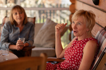 Lifestyle photo of two women sisters 55 years old, patio wooden house