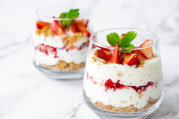 Strawberry dessert with cream cheese or yogurt, granola and fresh strawberry in glass on marble background. Recipe of simple healthy homemade organic dessert, cheesecake, mousse or berry trifle.