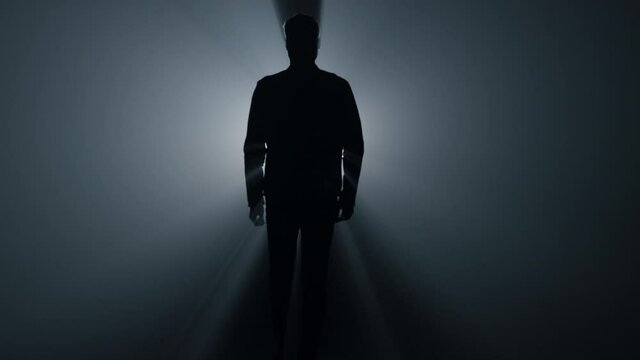 Silhouette man walking in darkness. Male person going straight on in dark.