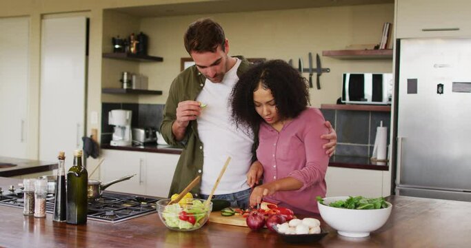 Happy diverse couple preparing food together in kitchen, chopping vegetables for salad
