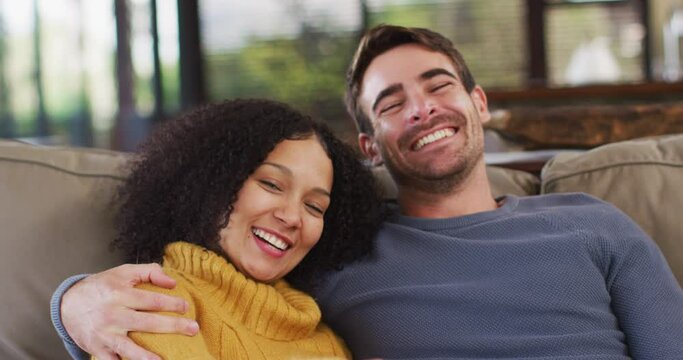 Portrait of happy diverse couple sitting on couch in living room, embracing and smiling