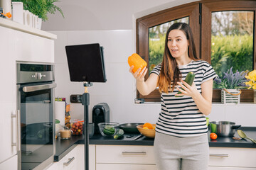 Fototapeta na wymiar Food blogger shows a bell pepper online using a tablet. Stream online from the kitchen when a woman is cooking. Prepare healthy food online 