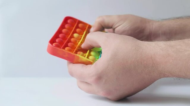 Male hands are playing with a rainbow Pop It Toy on a white background. Fashionable colorful anti-stress fidget bubble popping toy. Close-up