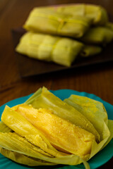 Uma porção de pamonhas amarradas na palha de milho e uma pamonha aberta e pronta para o consumo.