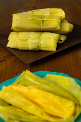 Uma porção de pamonhas amarradas na palha de milho e uma pamonha aberta e pronta para o consumo.