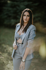 Pretty Caucasian lady wearing a gray crop top and blazer and posing in the park