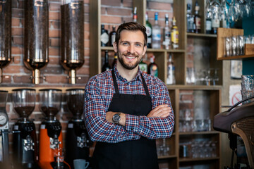 Waiter at the restaurant. The handsome server wears a plaid t shirt and apron. He has his arms...