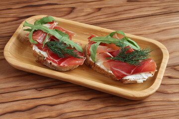 Buckwheat toasts with goat cheese, ham and arugula lying on a bamboo plate on a wooden table. Closeup